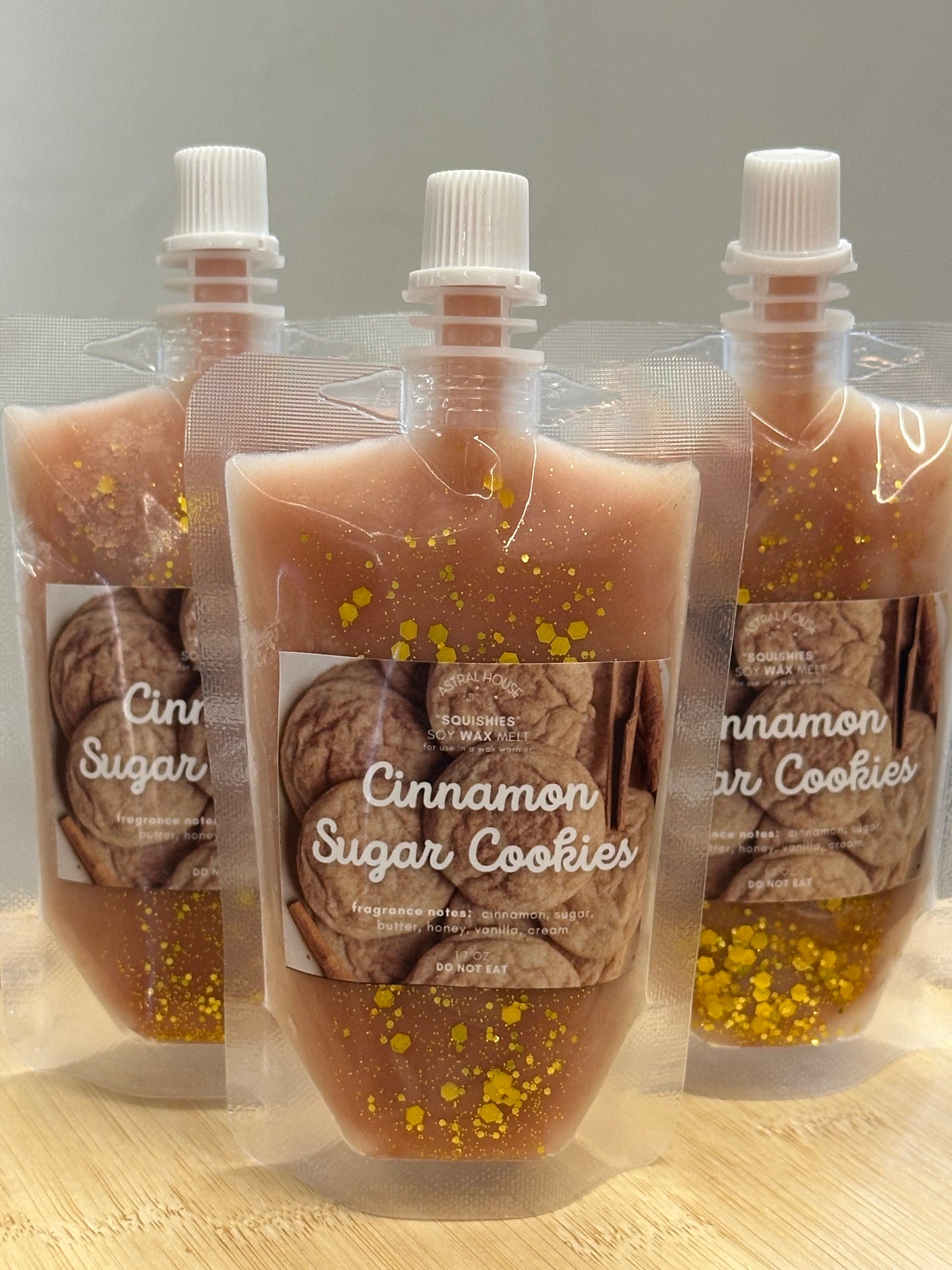 Transparent pouch with light brown colored wax adorned with gold glitter.  Square label with a photo of cinnamon sugar cookies on a light wooden surface.  Reads “Cinnamon Sugar Cookies” in a cursive font.